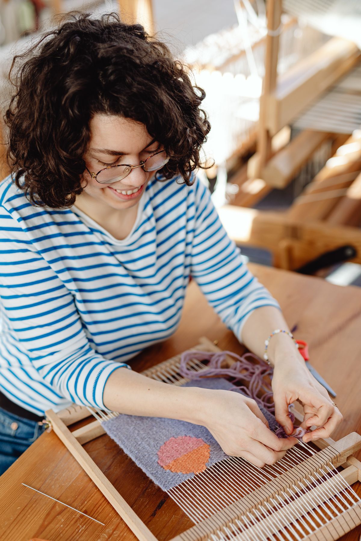 Weaver working coloured wool on a wooden loom at a table