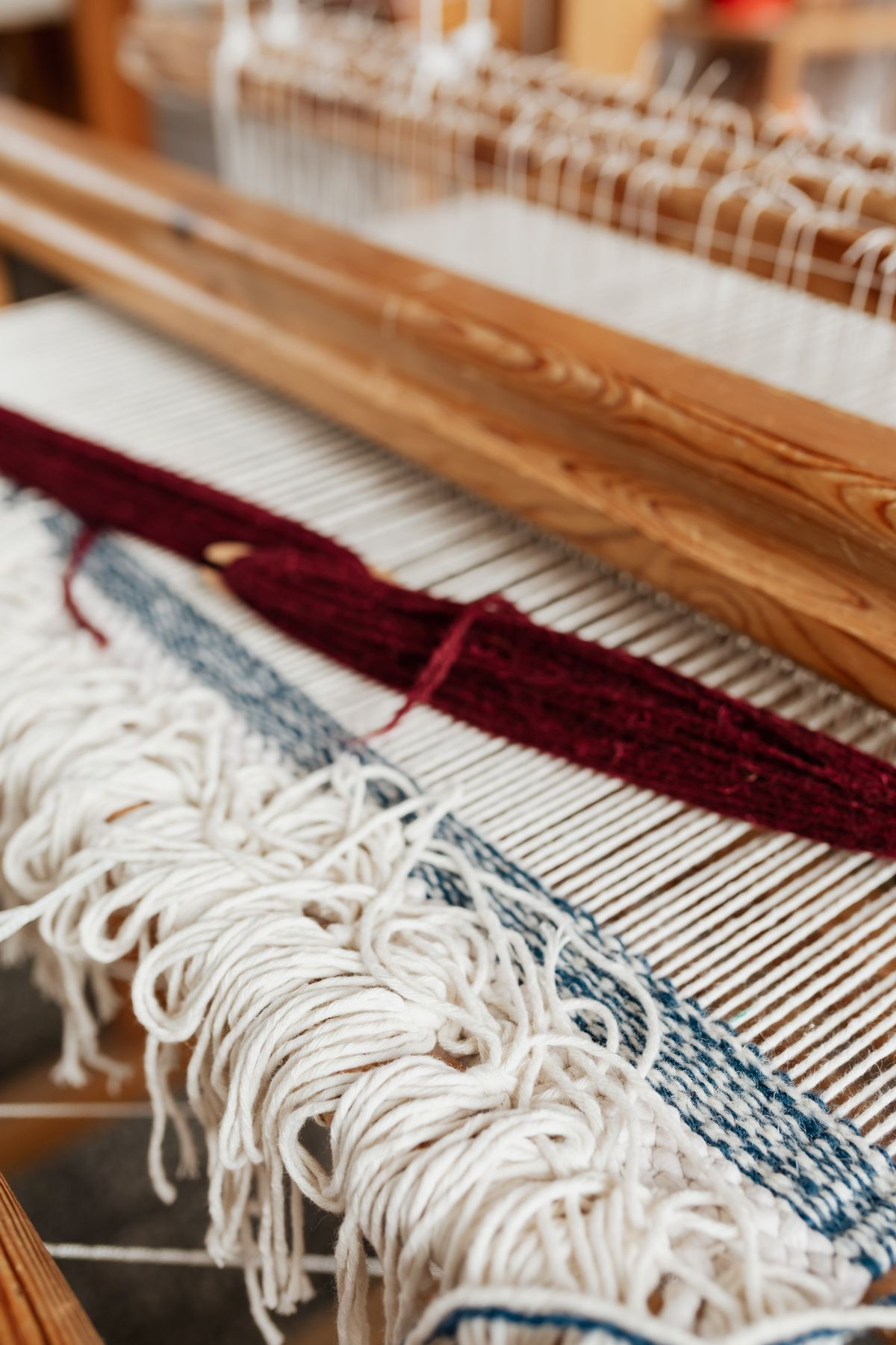 Hand-woven wool in cream, red and navy stretched across a wooden loom