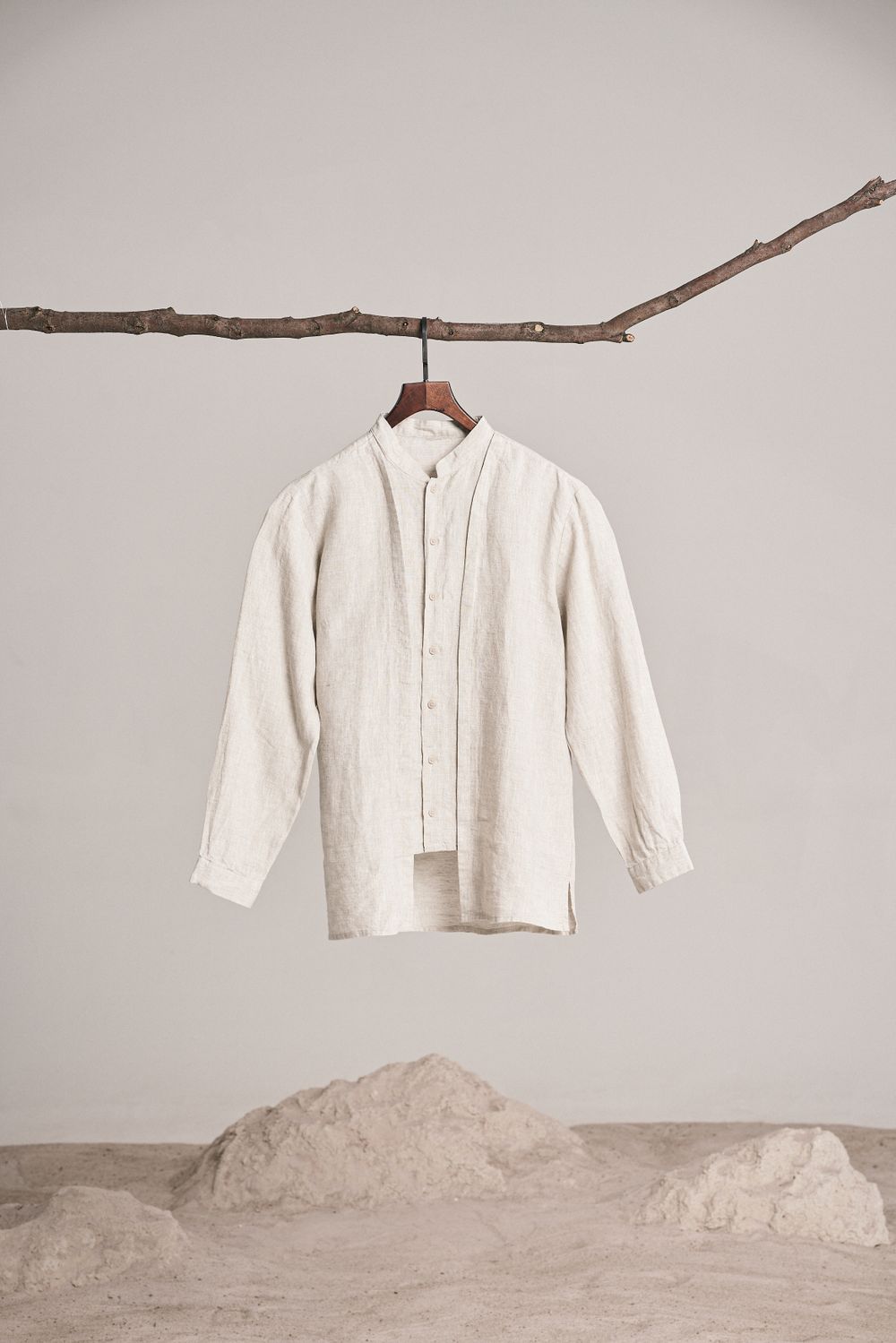 A natural linen shirt hanging from a branch against a pale wall