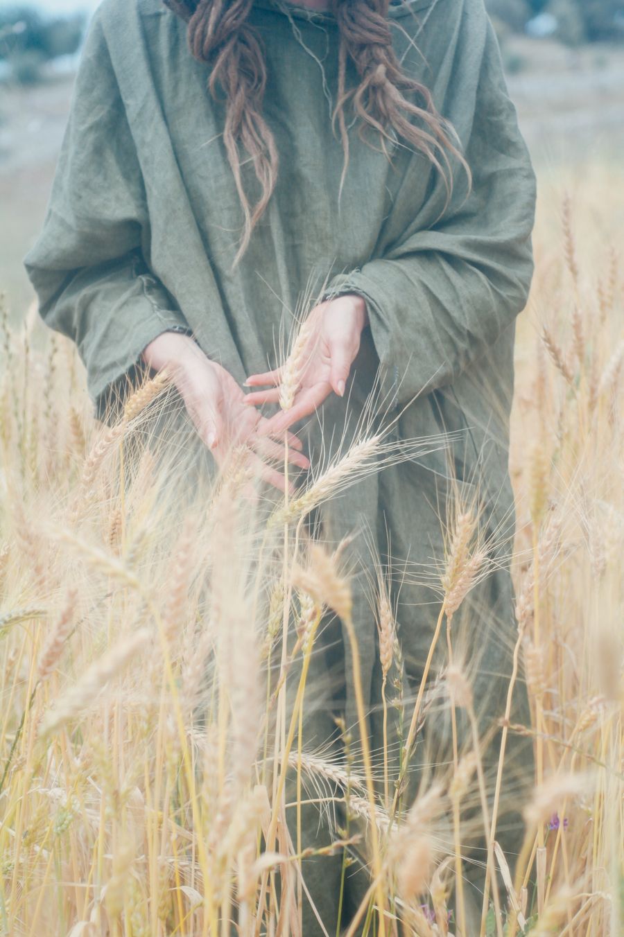 Close-up of hands resting on a green linen dress among wheat